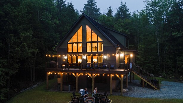 A large wooden cabin with a balcony and deck, surrounded by trees.