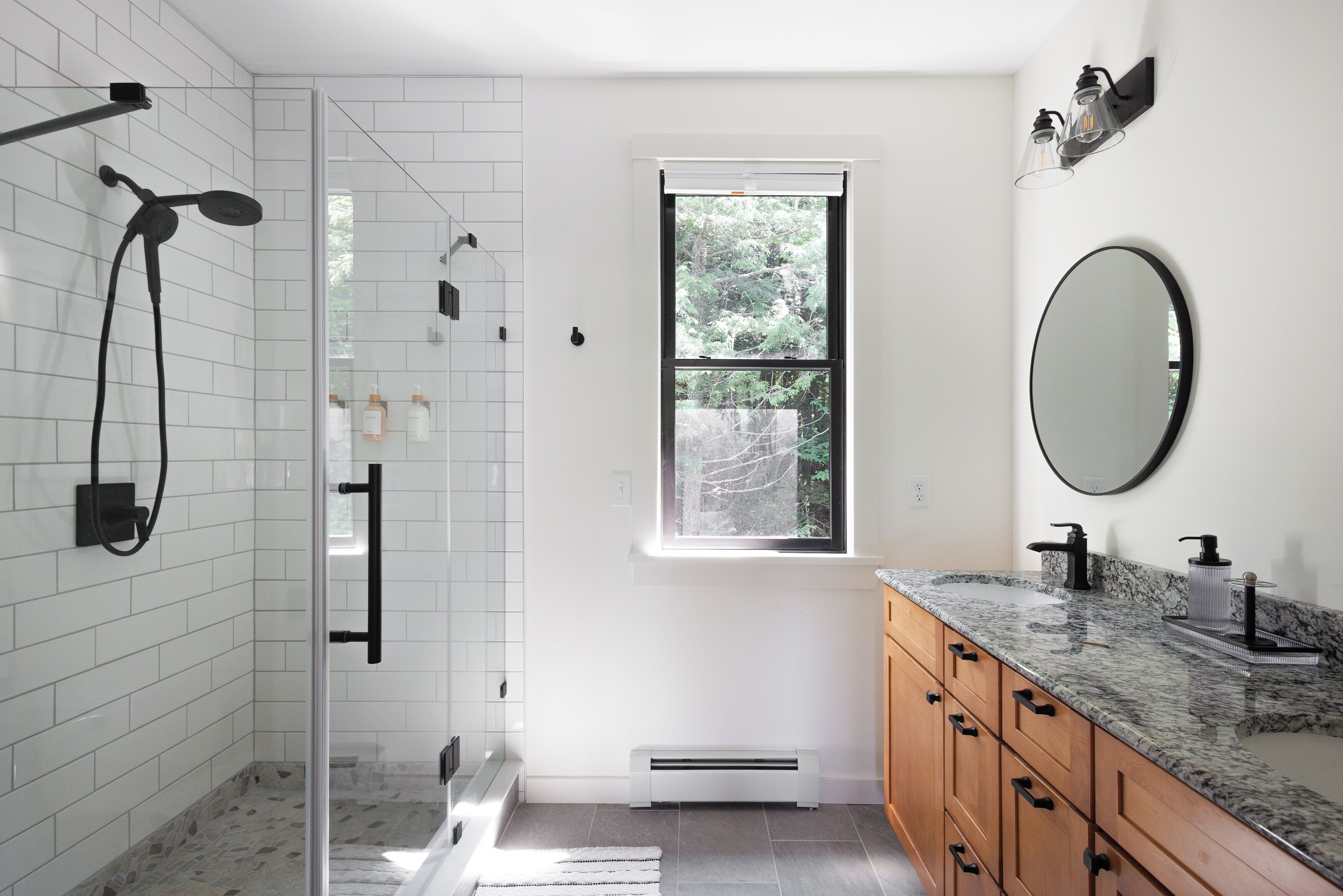 Une salle de bain moderne dotée d’une douche à parois de verre, d’une grande fenêtre, d’un comptoir en marbre et d’armoires en bois.