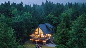 A lodge with a large deck and outdoor seating area, surrounded by dense forest.