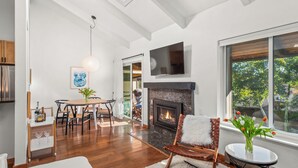 A spacious living room with a fireplace, wooden flooring, and a large window offering a view of the outdoors. - Chic Mountain Getaway on Shuttle Route (Snowmass Village)