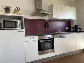 Una cocina moderna con armarios blancos, microondas, estufa y cafetera.