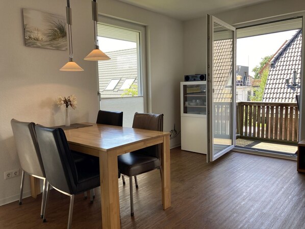 A dining area with a wooden table and chairs, a white refrigerator, and a sliding glass door leading to a balcony. - Kellenhusen - Meeresbrise - "Meeresbrise" on foot in less than 5 minutes from the (Kellenhusen (Ostsee))