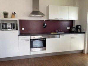 A modern kitchen with white cabinets, a stainless steel oven, a microwave, and a coffee maker. - Kellenhusen - Meeresbrise - "Meeresbrise" on foot in less than 5 minutes from the (Kellenhusen (Ostsee))
