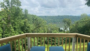 A wooden deck with a railing, two blue cushioned benches, and a view of a lake surrounded by trees. - Breathtaking Views of Dale Hollow Lake (Monroe)