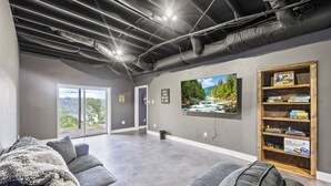 A modern living room with a gray couch, a large flat-screen TV mounted on the wall, and a wooden bookshelf. - Breathtaking Views of Dale Hollow Lake (Monroe)