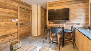 Una cocina moderna con paredes de madera, un televisor grande, taburetes de bar y un lavamanos.