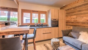 Una cocina moderna con armarios de madera, un comedor con mesa y sillas, y un sofá gris con un plaid suave.