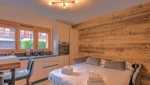 Un dormitorio con pared de madera, una cama con almohadas, una mesita de noche y un ventanal con vistas al verdor.