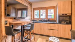 Una cocina moderna con armarios de madera, una zona de bar con taburetes y un amplio ventanal que proporciona luz natural.