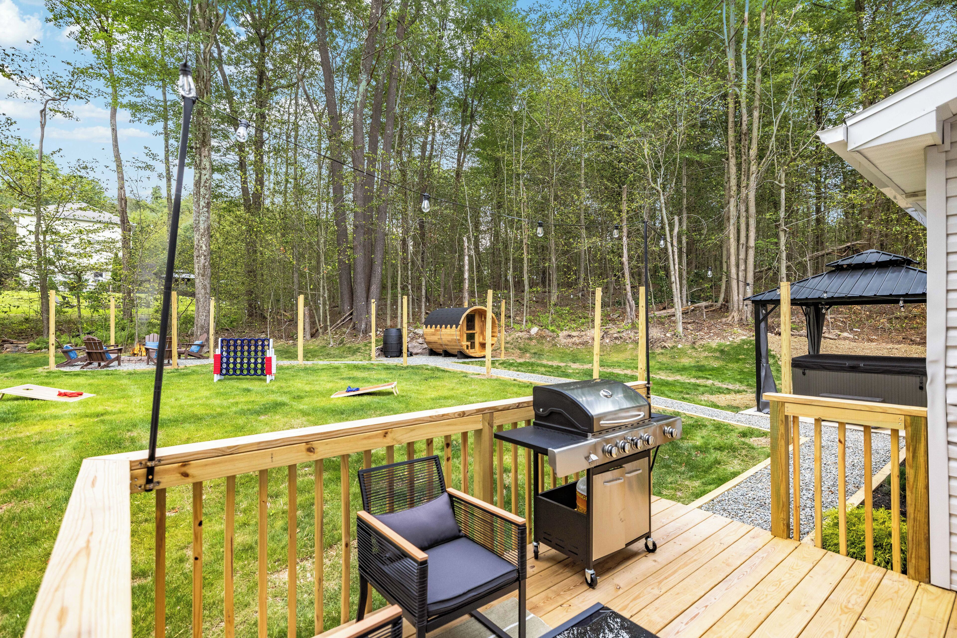 Une terrasse en bois avec un barbecue, une chaise et un jacuzzi, le tout situé dans un espace boisé.
