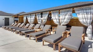 Une rangée de chaises longues avec des coussins gris, des structures en bois et des rideaux à rayures.