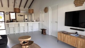 Una sala de estar moderna con un televisor grande, una consola de madera y una cocina con taburetes de bar.