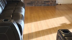 Un salon avec une cheminée en briques, un canapé en cuir noir, un téléviseur à écran plat et un plancher en bois.