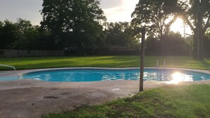 Un jardin à l’arrière de la maison, avec une piscine, entouré d’une clôture en bois et d’arbres.