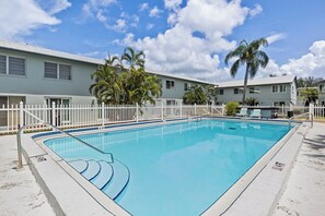 Une piscine rectangulaire entourée d’une clôture blanche, avec en arrière-plan un bâtiment doté de nombreuses fenêtres et un ciel dégagé.