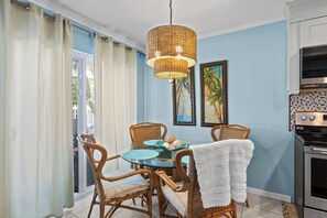 A dining area with wicker chairs, a glass table, and a hanging light fixture.