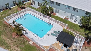 Ein rechteckiger Swimmingpool mit weißem Zaun, umgeben von Gras und Palmen.