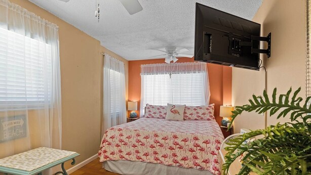 A bedroom with a bed, a TV mounted on the wall, a ceiling fan, and a window with sheer curtains. - 10125 Coral Coconut Cay - Condominium 2 Bedroom / 2 1/2Bath waterfront, maximum occupancy of 6 people. Community pool. (Bradenton)