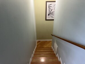 Eine Holztreppe mit weißem Zierrahmen und einer Handlauf, die zu einem Zimmer mit hellgrünen Wänden und einem gerahmten, abstrakten Kunstwerk führt.