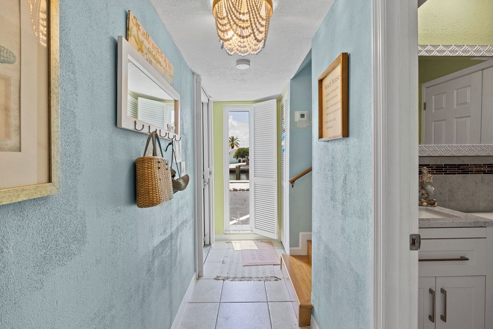 A hallway with a view to the outside, a hanging basket, and a door leading to a room.