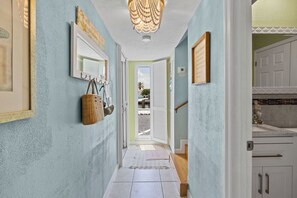 A hallway with a view to the outside, a hanging basket, and a door leading to a room.
