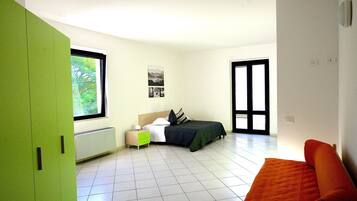 A bedroom with a bed, a nightstand, a green wardrobe, a window, and a door.