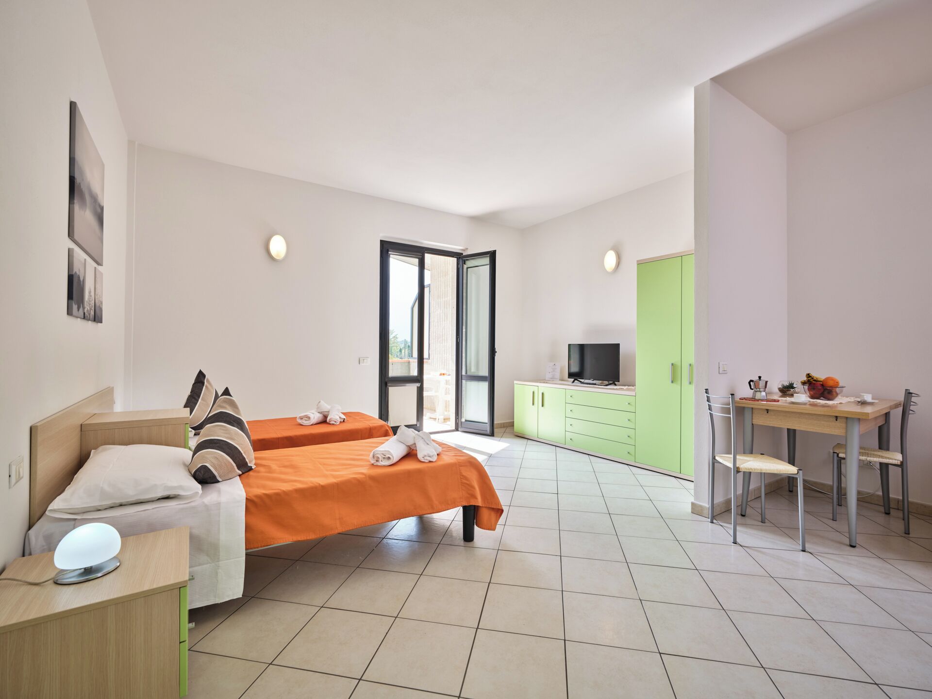 A modern bedroom with two beds, a desk, and a television.