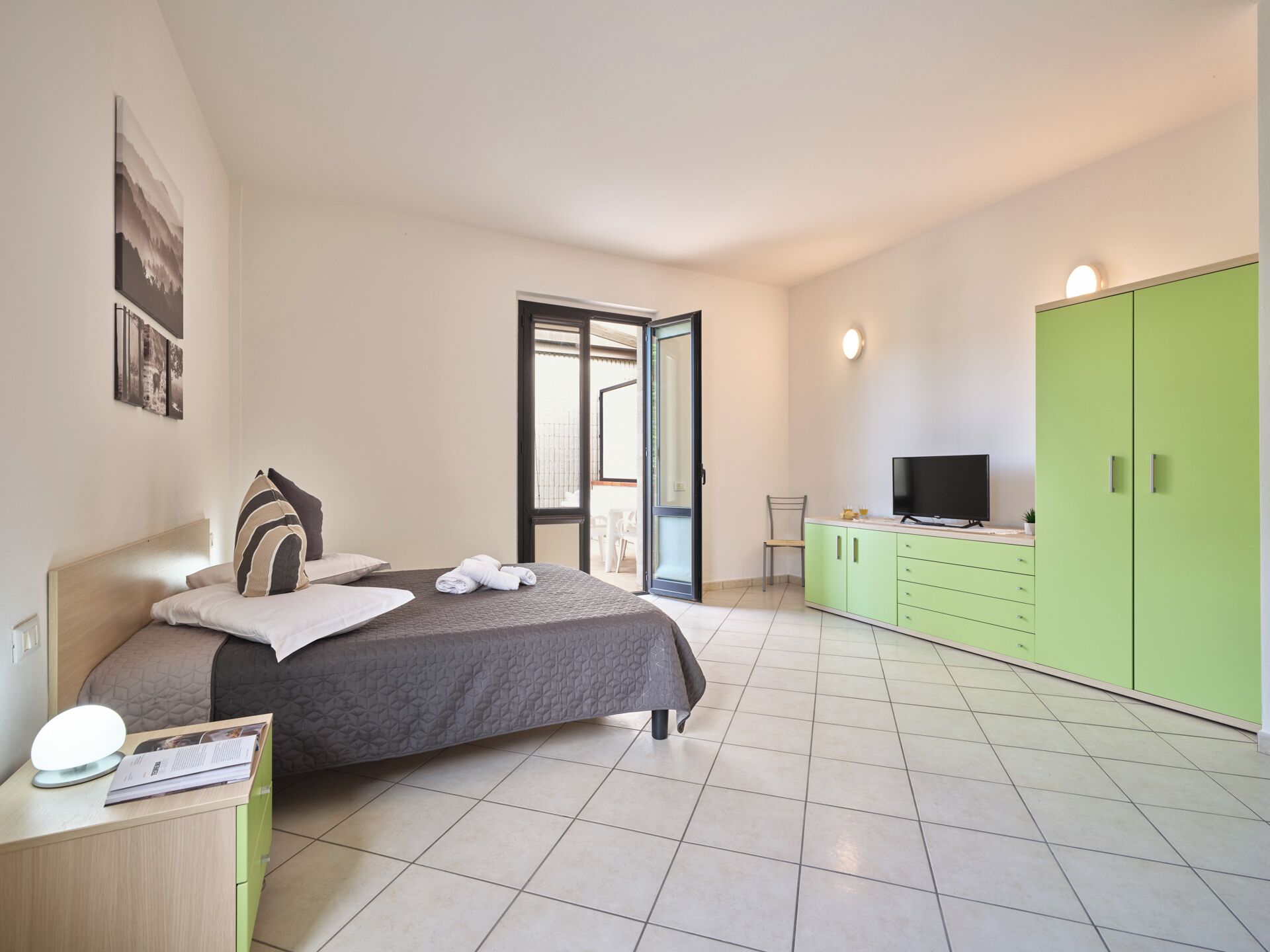 A bedroom with a bed, a TV, a green wardrobe, and a bathroom visible through an open door.