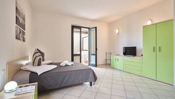 A bedroom with a bed, a TV, a green wardrobe, and a bathroom visible through an open door.