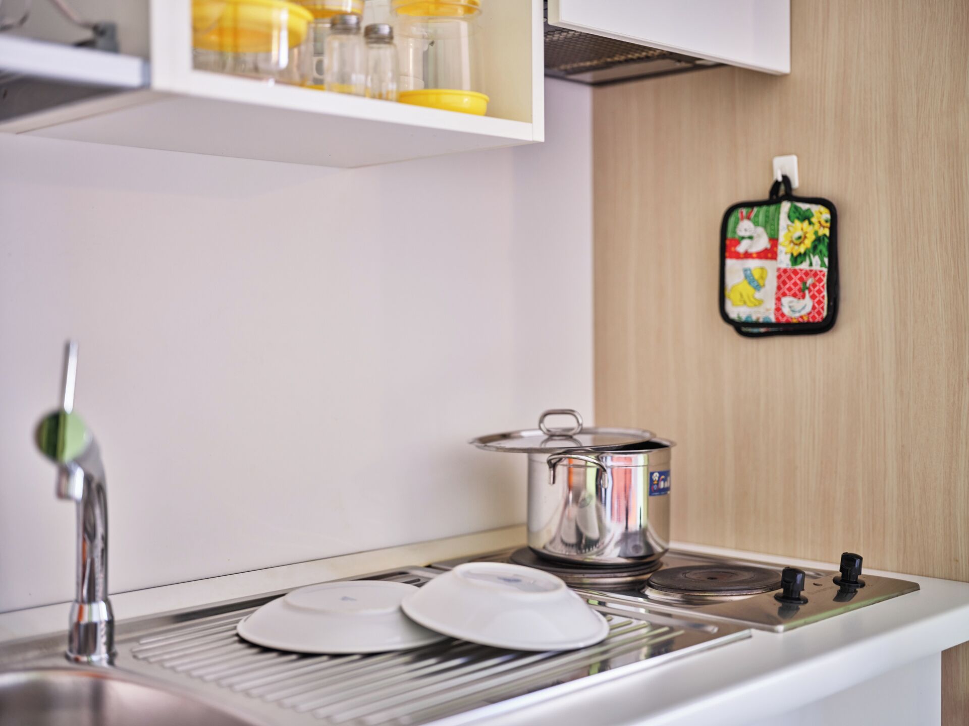 A kitchen with a stainless steel sink, a stove, and a pot on the counter.