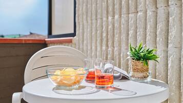 Una mesa blanca con un cuenco de aperitivos, dos vasos de jugo de naranja y una pequeña planta en maceta en un balcón.