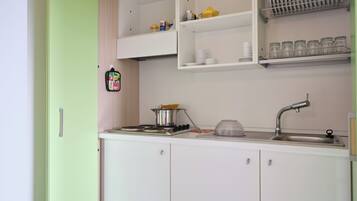 A kitchen with white cabinets, a sink, and a stove. There are shelves above the stove holding dishes and jars.