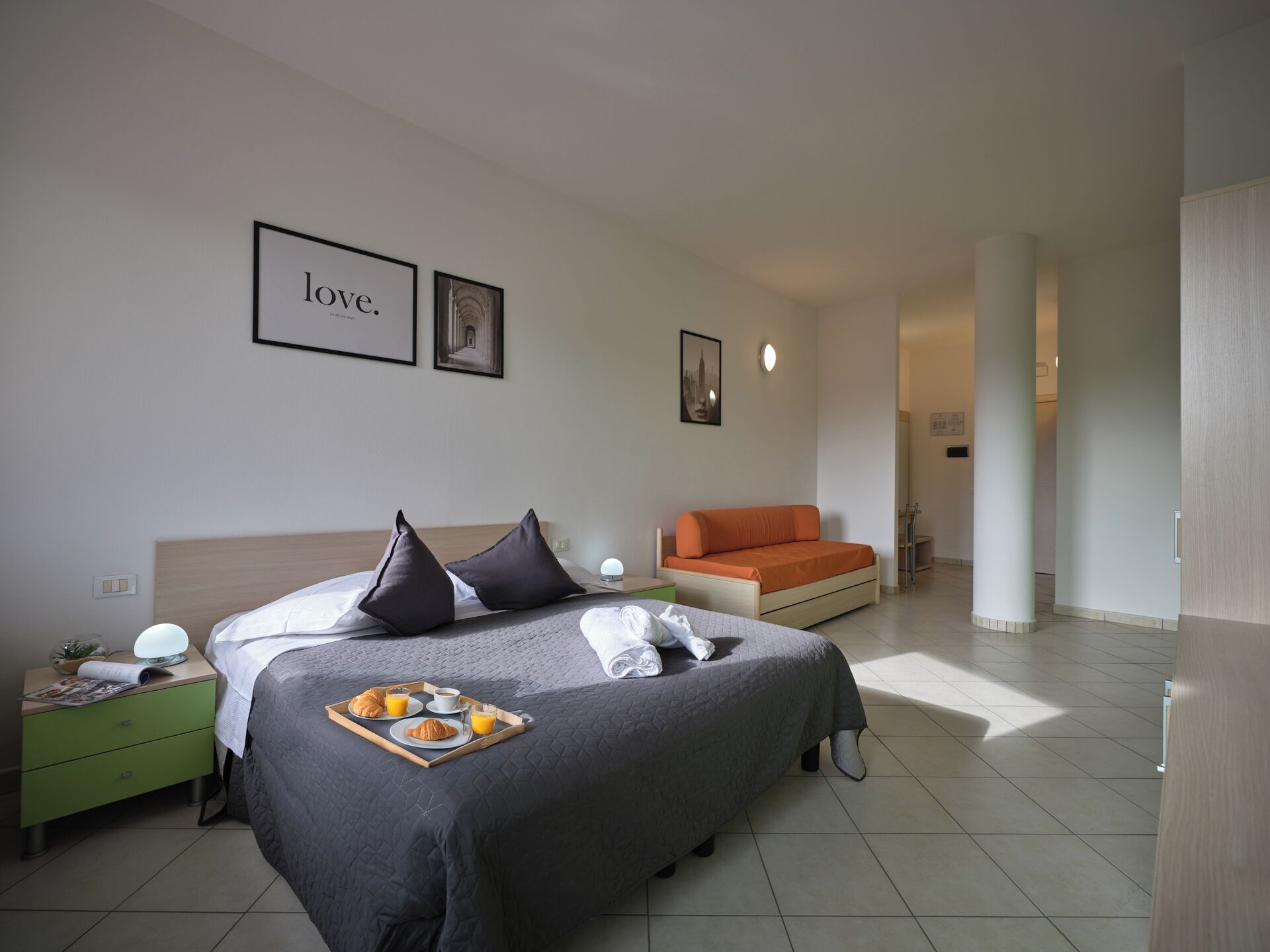 Een moderne hotelkamer met een groot bed, een bank en een ontbijtplateau op het bed.