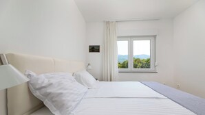 A hotel room with a bed, a nightstand, a lamp, a window with a view of greenery, and a small painting on the wall. - Villa Opera (Kvarner - Povile) (Povile)