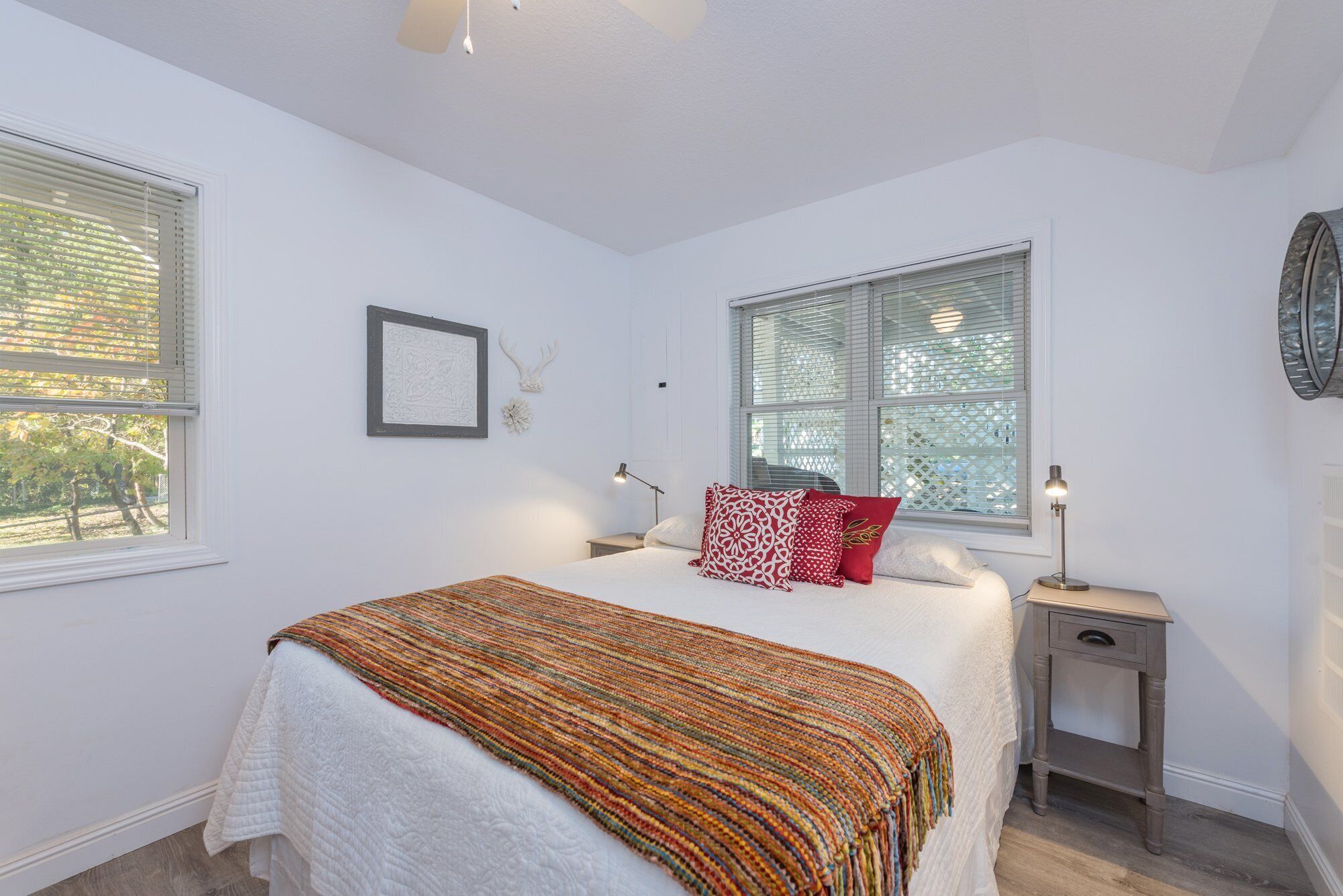 A bedroom with a bed, a bedside table, a lamp, a framed picture, and a window with blinds.