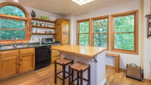 Une cuisine dotée de meubles en bois, d’un lave-vaisselle encastré, d’un grand îlot central avec des tabourets et de grandes fenêtres offrant une vue sur l’extérieur.