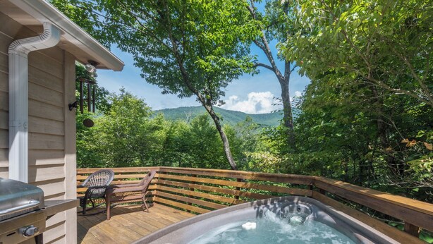 Un bain à remous sur une terrasse en bois, avec vue sur une forêt et des montagnes.