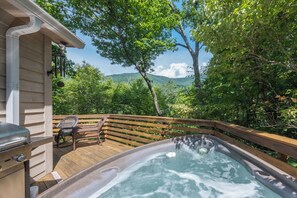 Un bain à remous sur une terrasse en bois, avec vue sur une forêt et des montagnes.