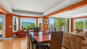 Une pièce spacieuse avec une grande table en bois, des sièges confortables et de grandes fenêtres offrant une vue sur les montagnes.