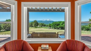 Une pièce dotée d’une grande fenêtre donnant sur les montagnes, de deux fauteuils à motifs et d’une petite table sur laquelle sont posés des livres.