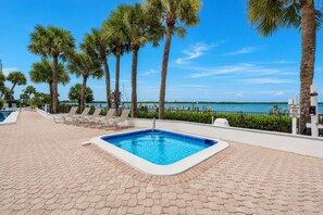 A swimming pool with lounge chairs, palm trees, and a view of the water.