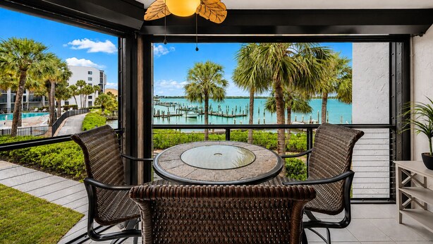 Un balcon avec une table et des chaises, un ventilateur de plafond et une vue sur un port de plaisance et une piscine.