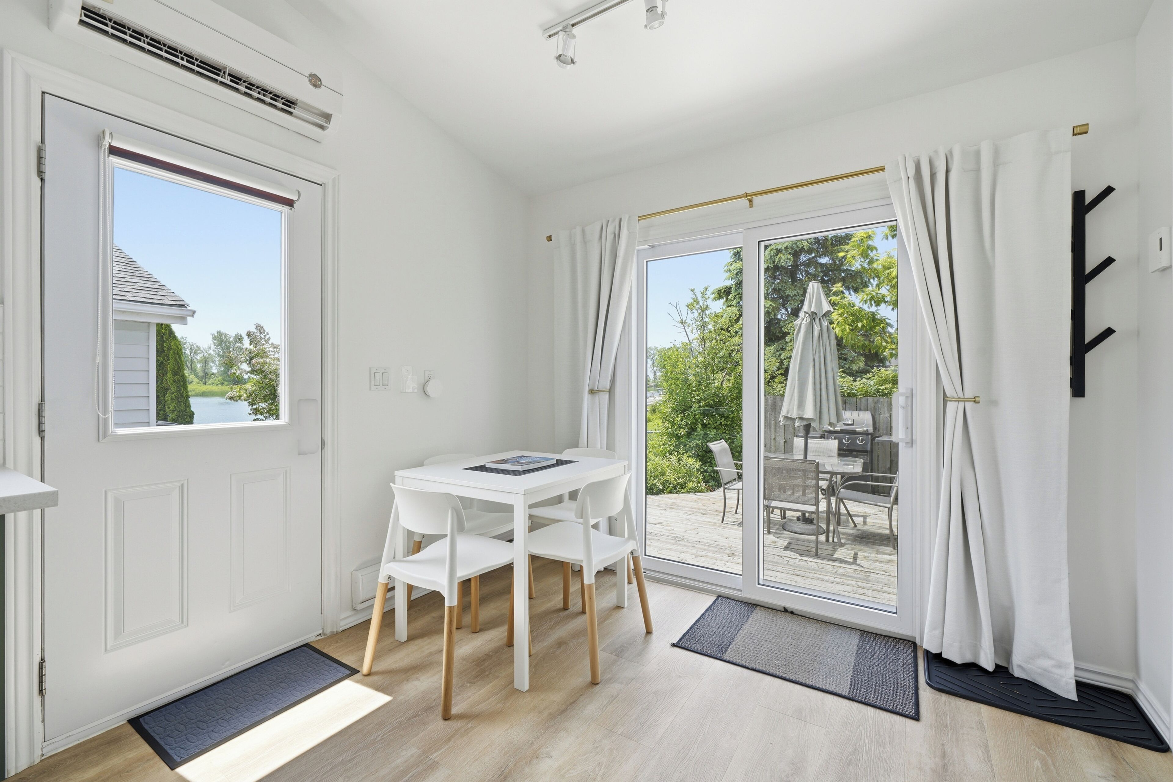 A room with a white door, a white table with chairs, a sliding glass door to an outdoor area, and a black coat rack.