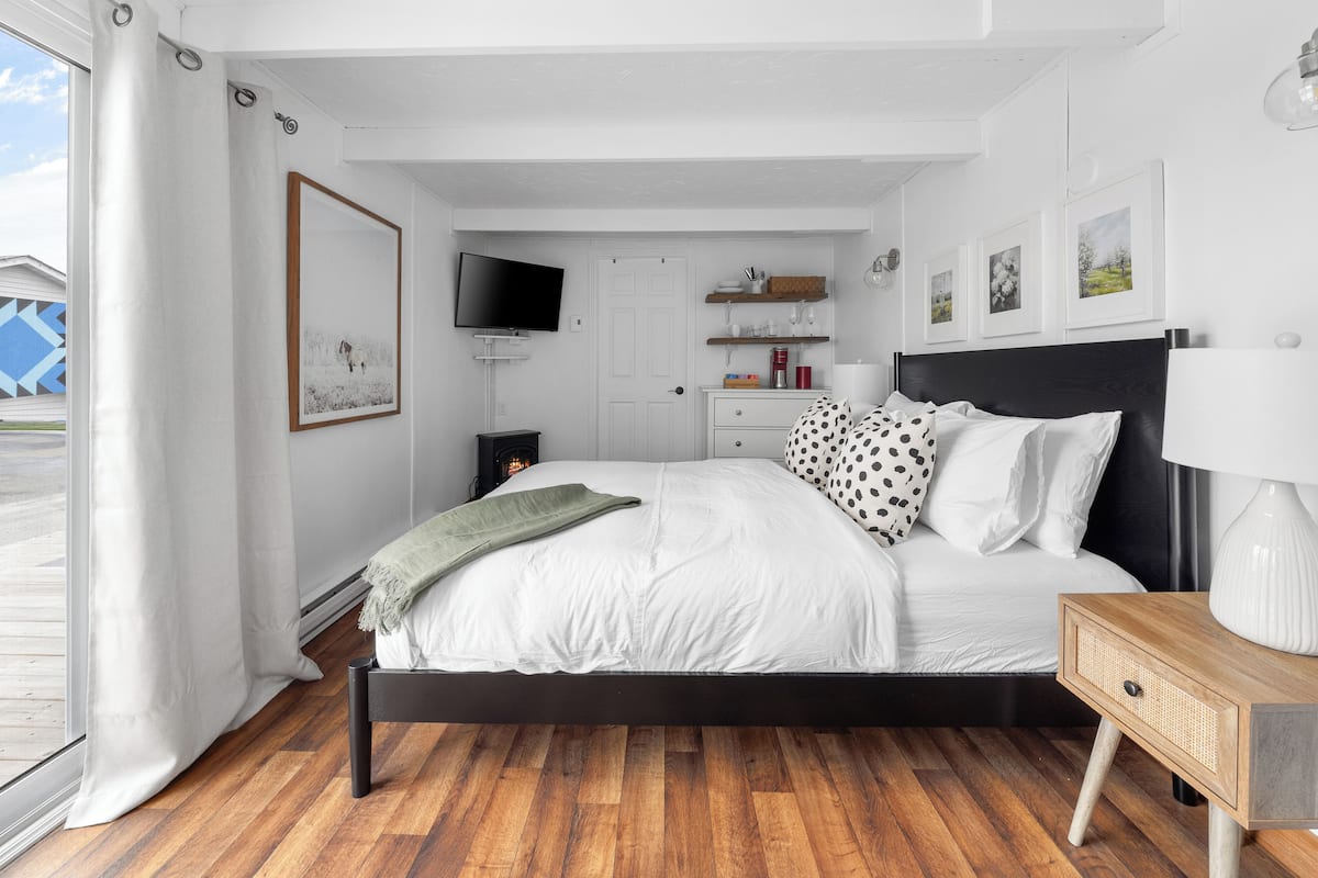 A bedroom with a bed, bedside table, TV, and a window with curtains.