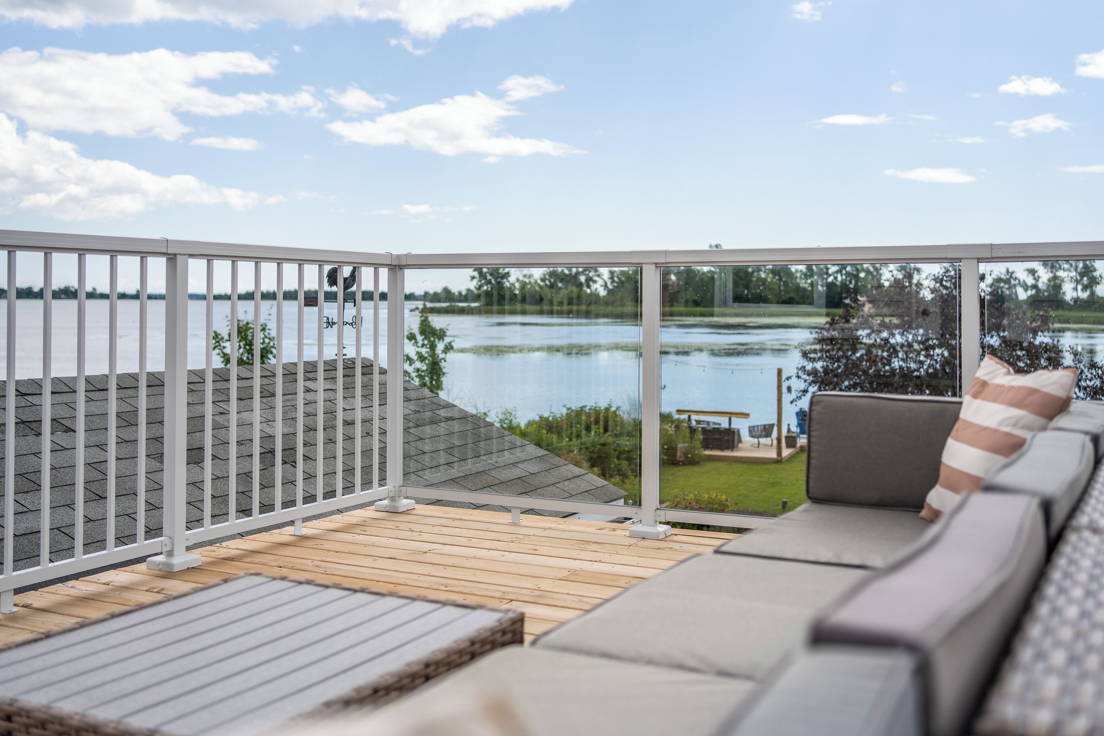 A deck with a view of a lake, a grassy area, and a building in the background.