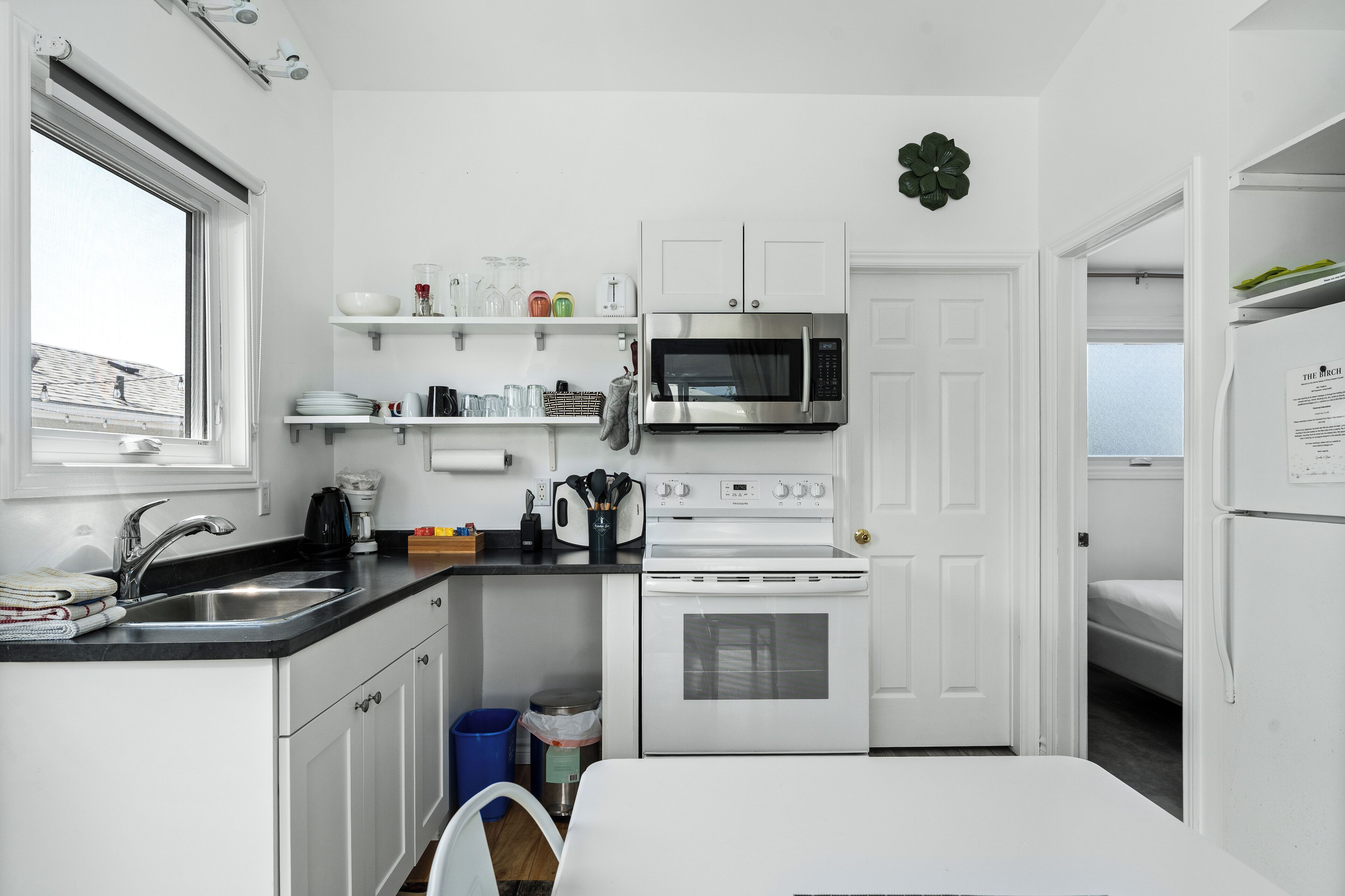 Cocina compacta con armarios blancos, microondas de acero inoxidable, horno empotrado y un lavabo con grifo.