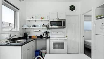 Cocina compacta con armarios blancos, microondas de acero inoxidable, horno empotrado y un lavabo con grifo.