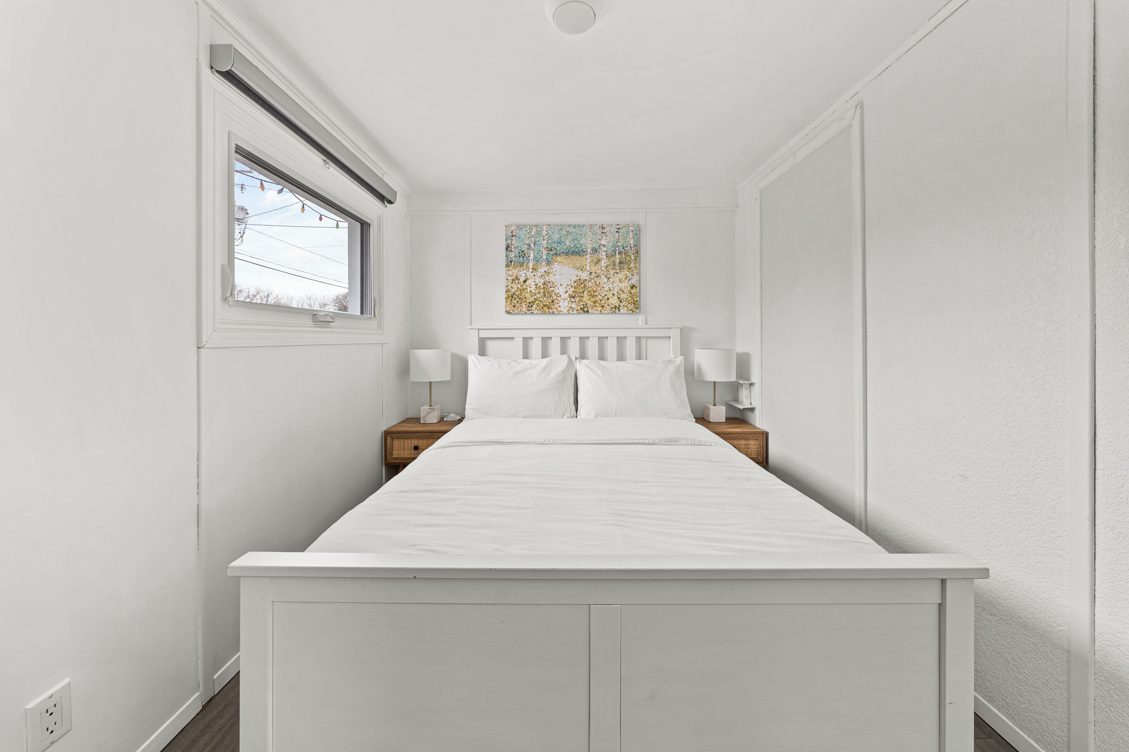A white bedroom with a bed, nightstands, and a painting on the wall.
