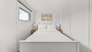 A white bedroom with a bed, nightstands, and a painting on the wall.