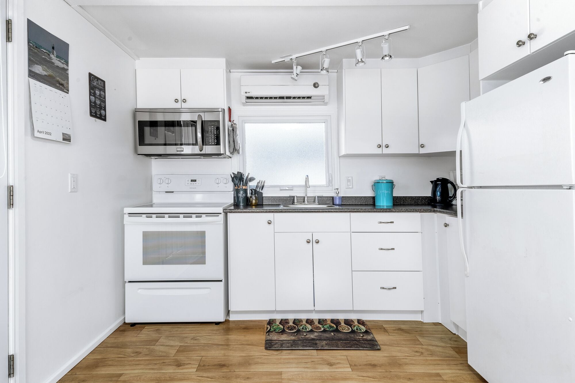 A modern kitchen with white cabinets, a stainless steel microwave, a stove, and a refrigerator.